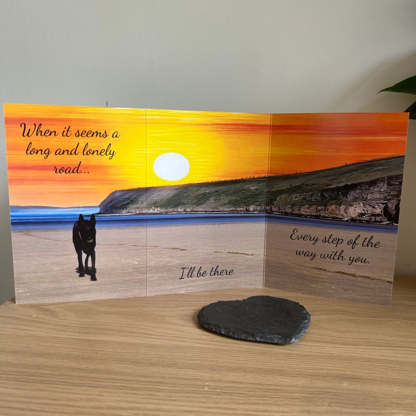 The image depicts a photo of the Bare Cards Sentiment Card 'Lonely Road' with the full trifold image open showing a dog on a deserted beach on a sunset background. The caption on the card reads 'When it seems a long and lonely road, I'll be there, every step of the way with you.'