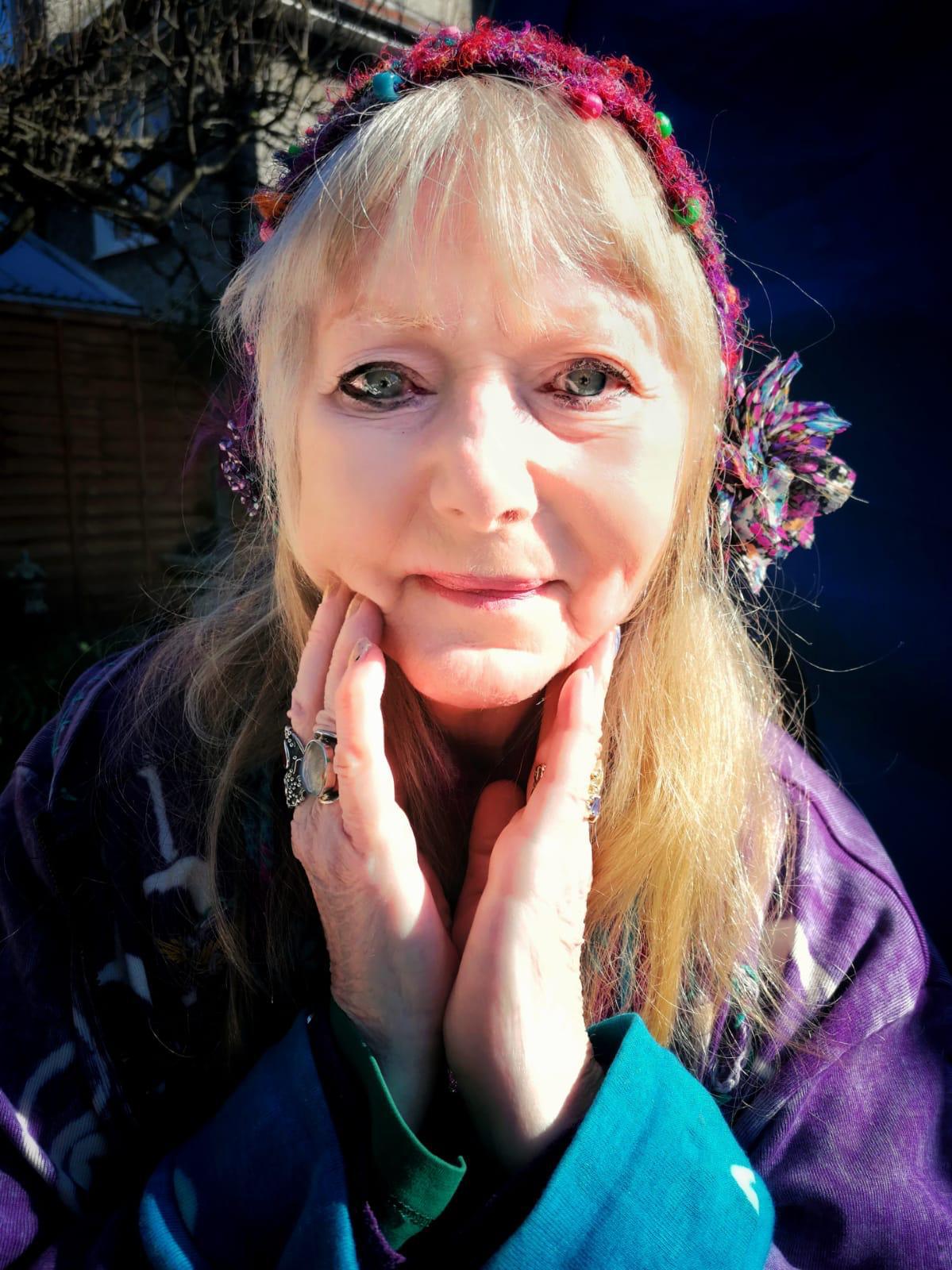 Portrait photograph of British Fantasy Artist Josephine Wall with decorative headband and colorful accessories posing outdoors in the sunshine