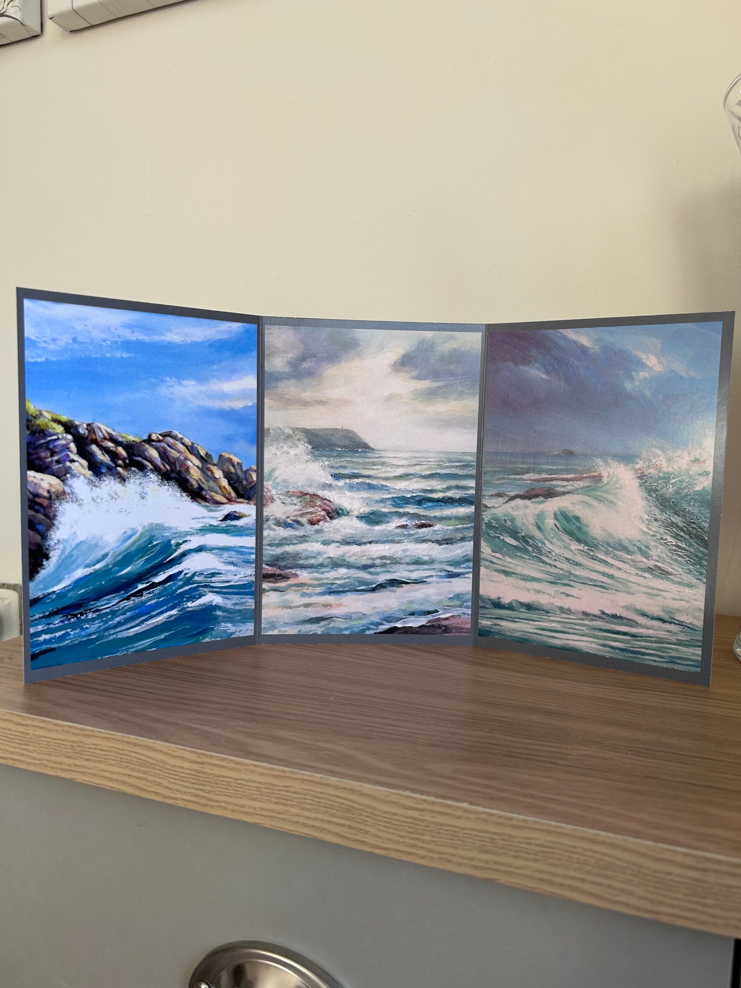 Self-sealing greetings card featuring Triptych paintings of ocean waves on a wooden surface with a plant in the background.