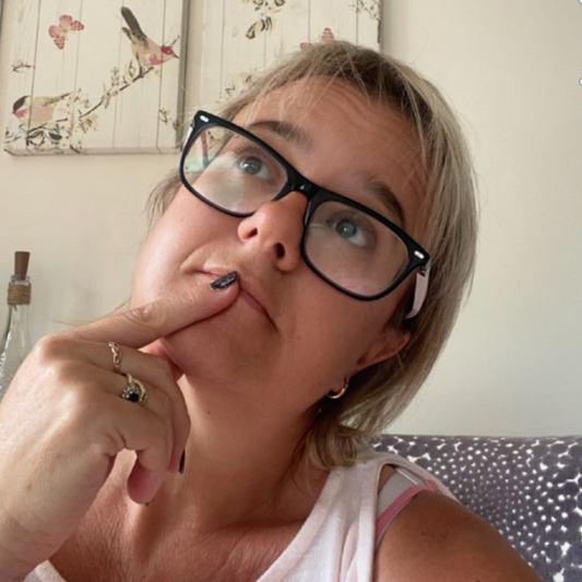 Photo shows Ceri Seal, owner of Bare Cards, in a pensive pose, looking up to the ceiling with a finger on her lip looking as though she is pondering the answer to a question. She is in her home setting.