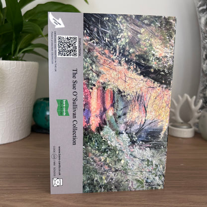 A photo of the back of the posting cover for  the self-sealing greetings card Autumn Leaves from 'The Sue O'Sullivan Collection' featuring a landscape painting of an autumn forest with yellow, green, and orange foliage on the right, and a beige sidebar on the left containing text, a QR code, and a green 'Bare Cards' logo.