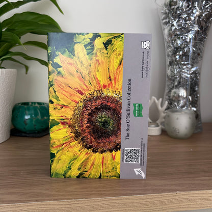 A photo featuring the back envelope panel of the self-sealing greetings card showing an abstract textured painting of a sunflower, with a beige side panel containing text, a QR code, and a green Bare Cards logo. The text reads 'The Sue O'Sullivan Collection'.