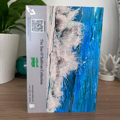 An photo featuring the back envelope panel of the self-sealing greetings card showing an abstract textured painting of a wave in shades of blue, white, and gray, with a beige side panel containing text, a QR code, and a green Bare Cards logo. The text reads 'The Sue O'Sullivan Collection'.
