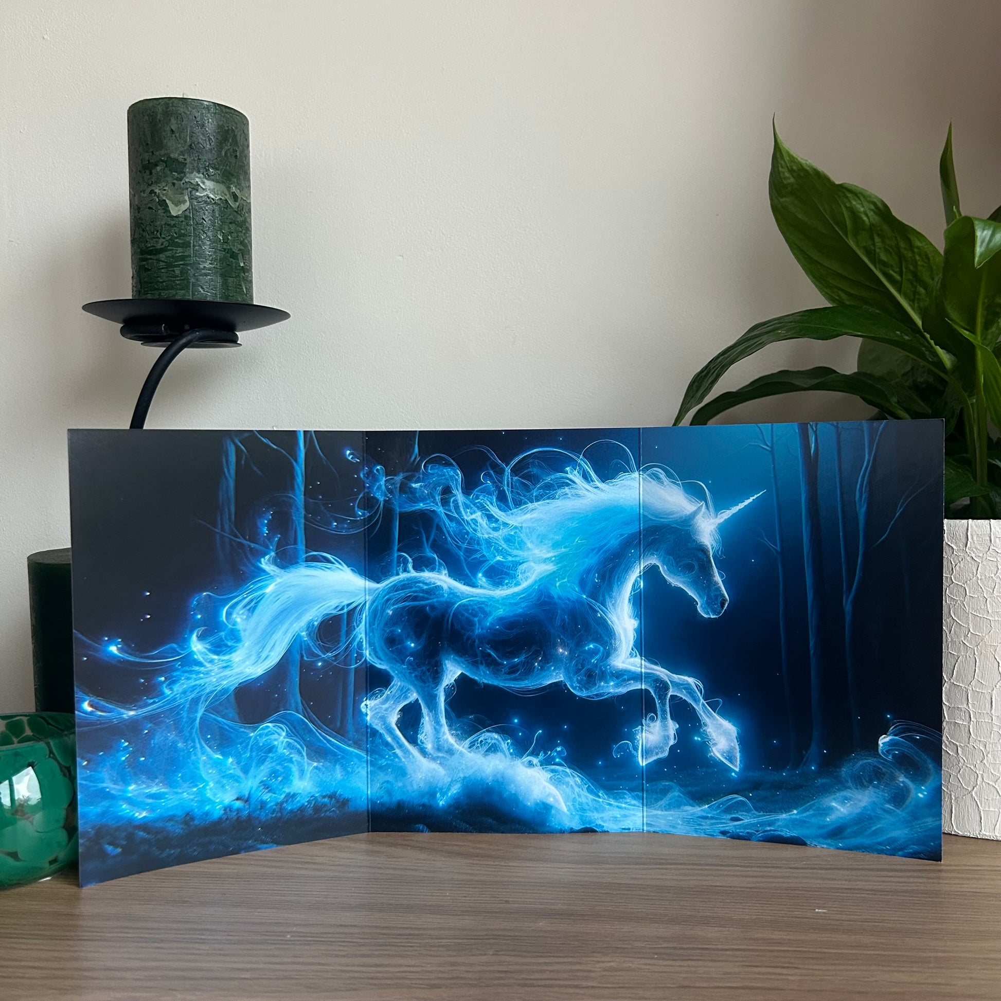 Blue unicorn artwork on a dark background with a candle and plant in the background