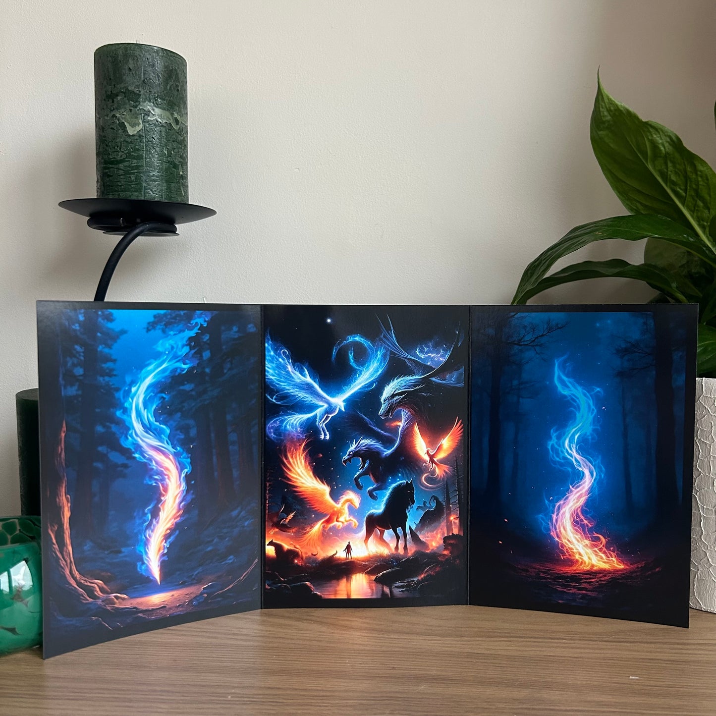 Triptych artwork with fantasy elements on a wooden surface with a candle and plant in the background.