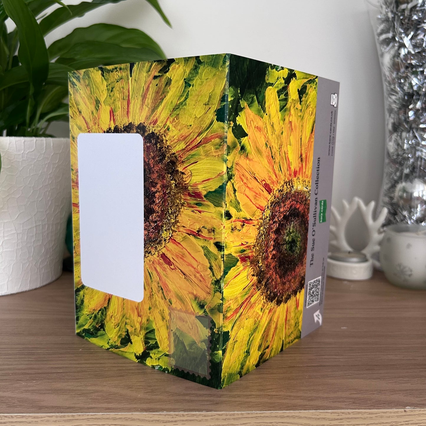 The posting covers of the Bare Cards Self-sealing greetings card - Flowers frm the Sue O'Sullivan collection, displayed on a wooden tabletop with a potted plant and decorative silver vase in the background. 