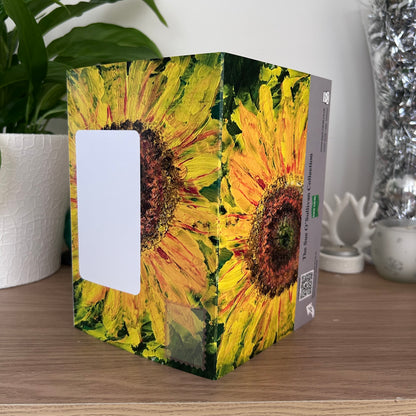 The posting covers of the Bare Cards Self-sealing greetings card - Flowers frm the Sue O'Sullivan collection, displayed on a wooden tabletop with a potted plant and decorative silver vase in the background. 