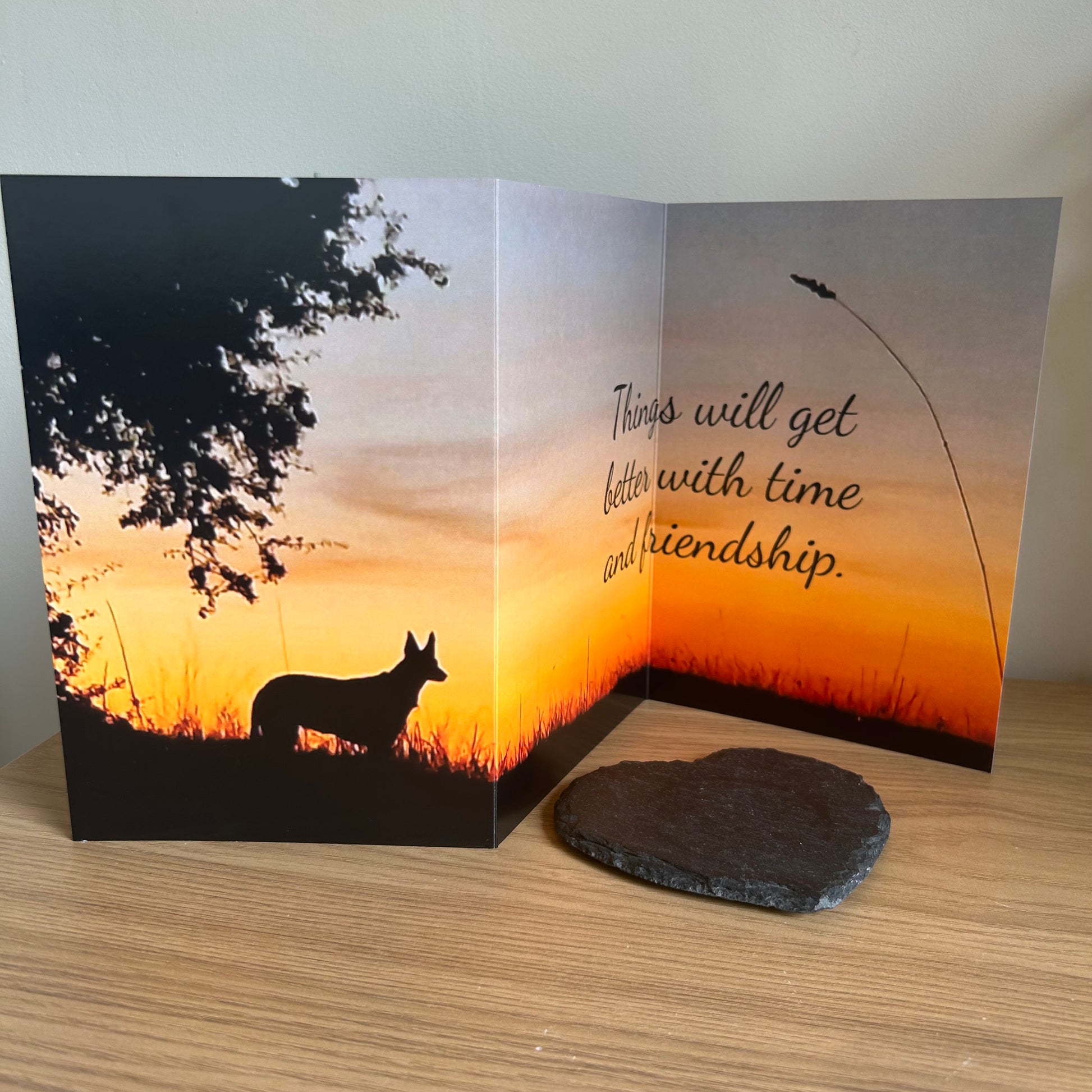 The image depicts a photo of the Bare Cards Dog Photo Sentiment Card with the full trifold image open showing a silhouette of a dog under a tree on a sunset background. The caption on the card reads 'Things will get better with time and friendship.'