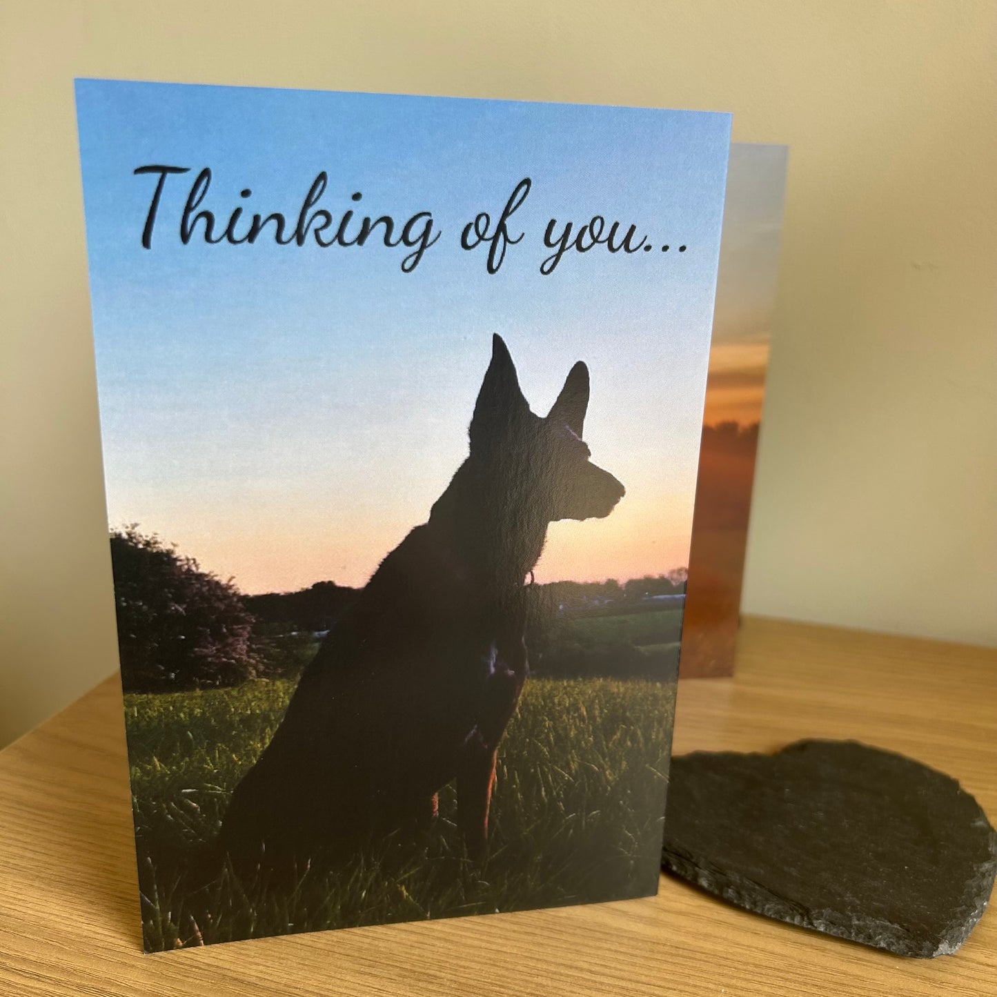 The image shows a photo of the front of the Bare Cards Dog Photo Sentiment Card 'Thinking of you' showing a black dog looking across the fields and the words 'Thinking of you...'.
