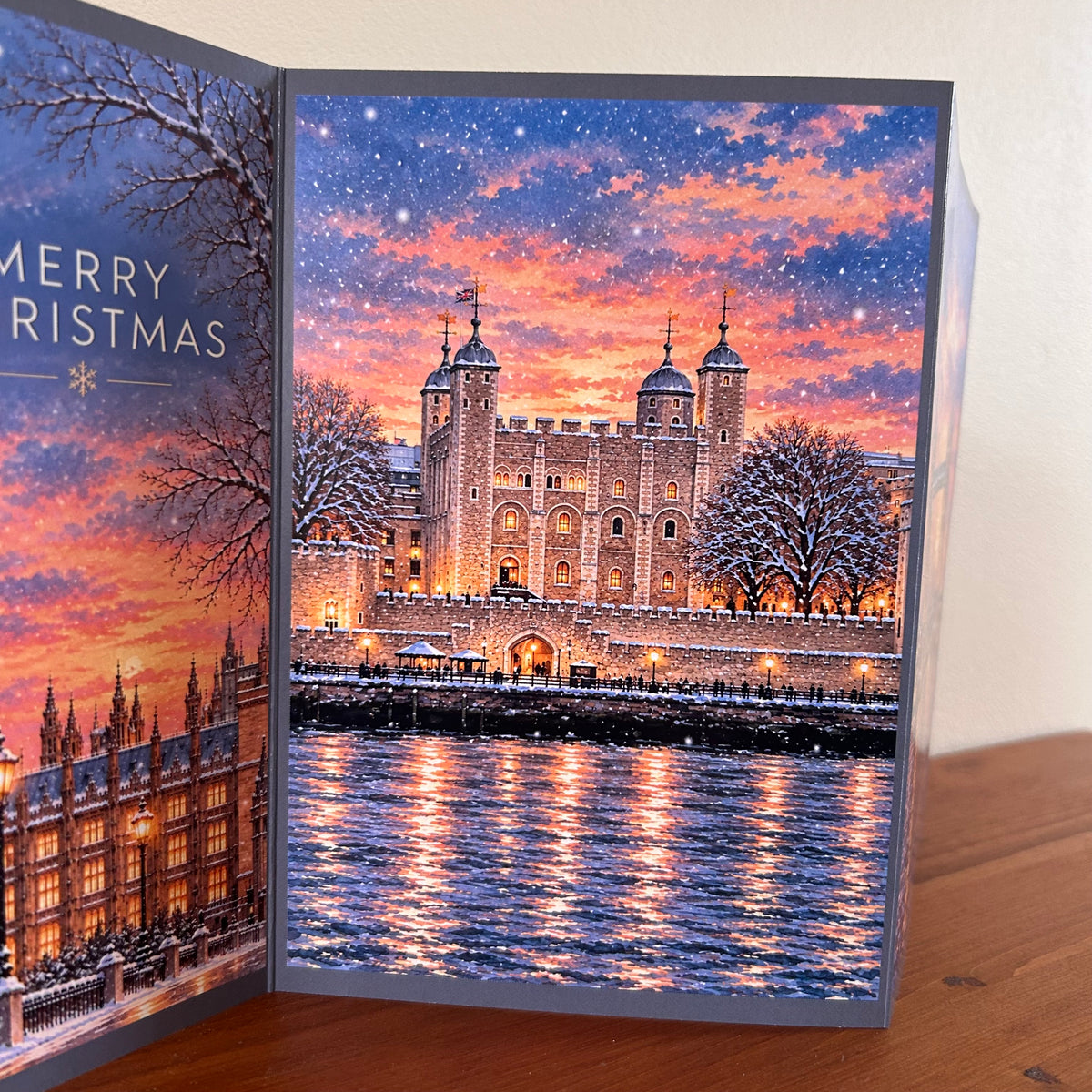 The middle panel of the Bare Cards triptych London Christmas greeting card featuring a festive Christmas scene with Tower Hill under a snowy orange and purple sky, displayed on a wooden surface.