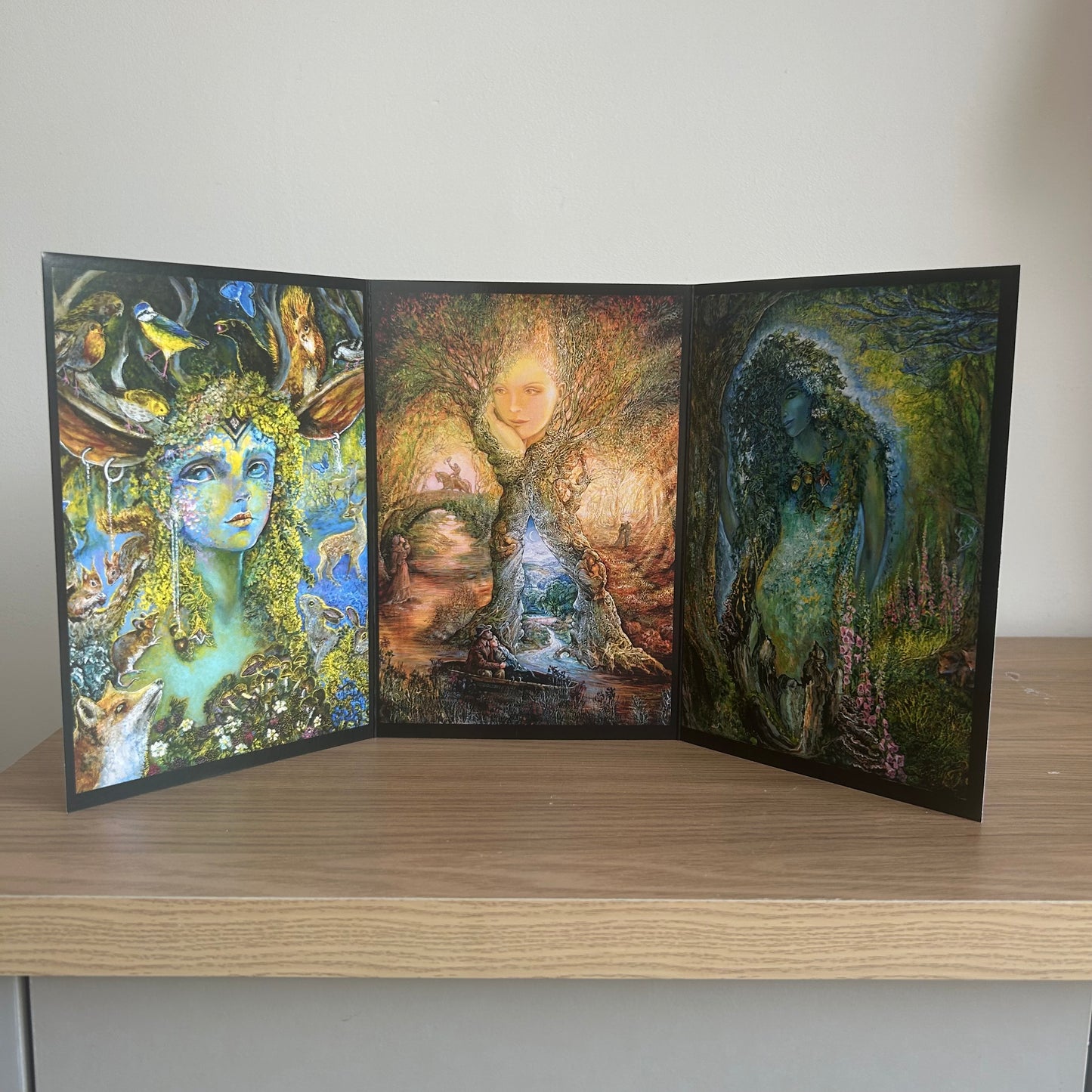Three-panel self-sealing greetings card UK with artistic fantasy designs featuring Josephine Wall paintings of nature and mystical figures on a wooden surface