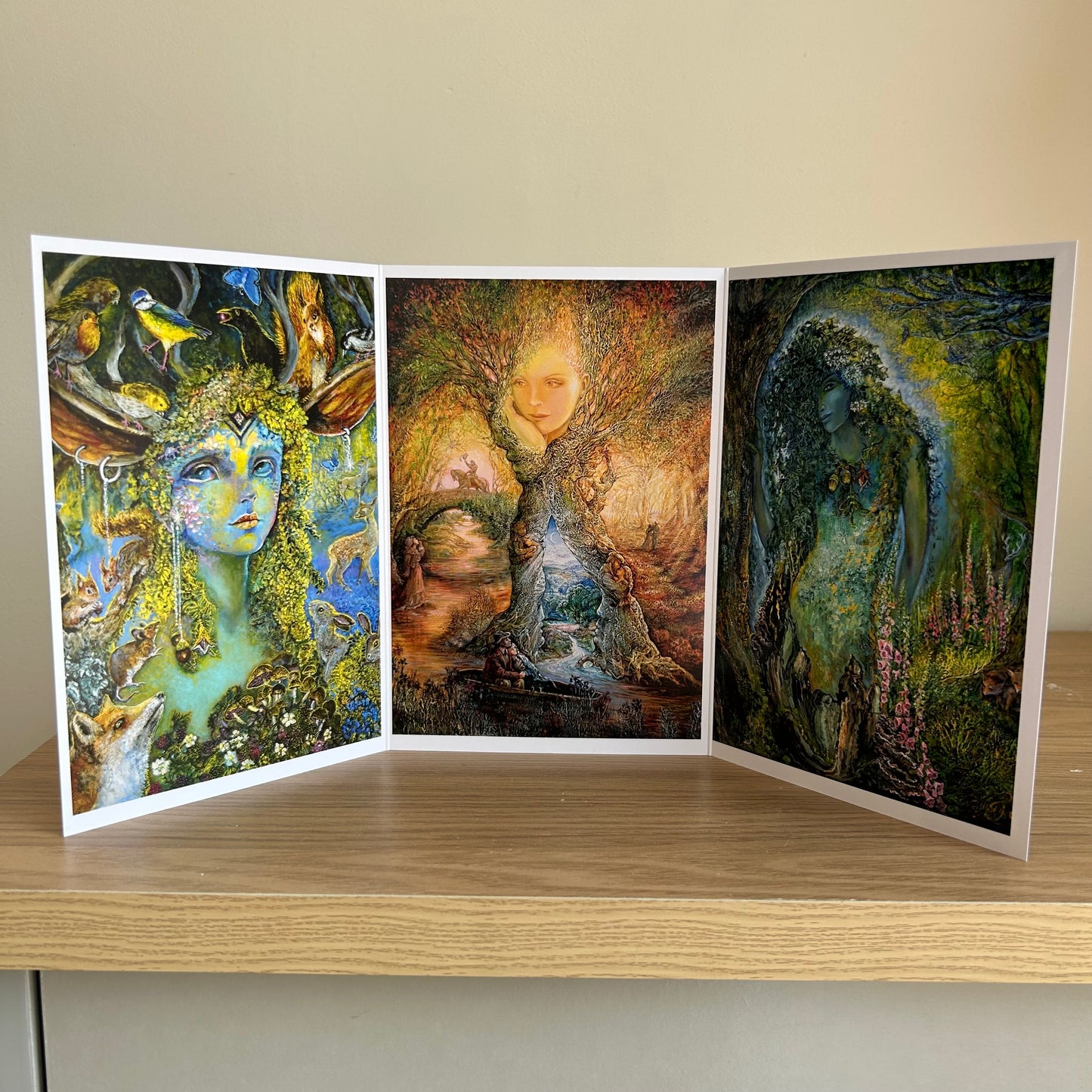 Three-panel self-sealing greetings card UK with artistic fantasy designs featuring Josephine Wall paintings of nature and mystical figures on a wooden surface
