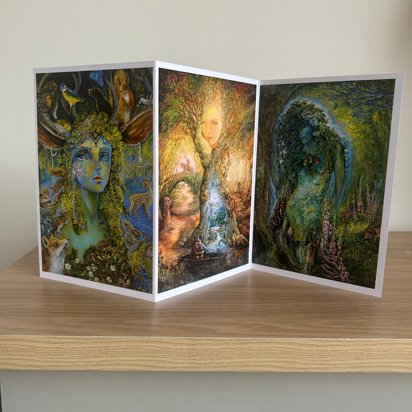 Three-panel self-sealing greetings card UK with artistic fantasy designs featuring Josephine Wall paintings of nature and mystical figures on a wooden surface