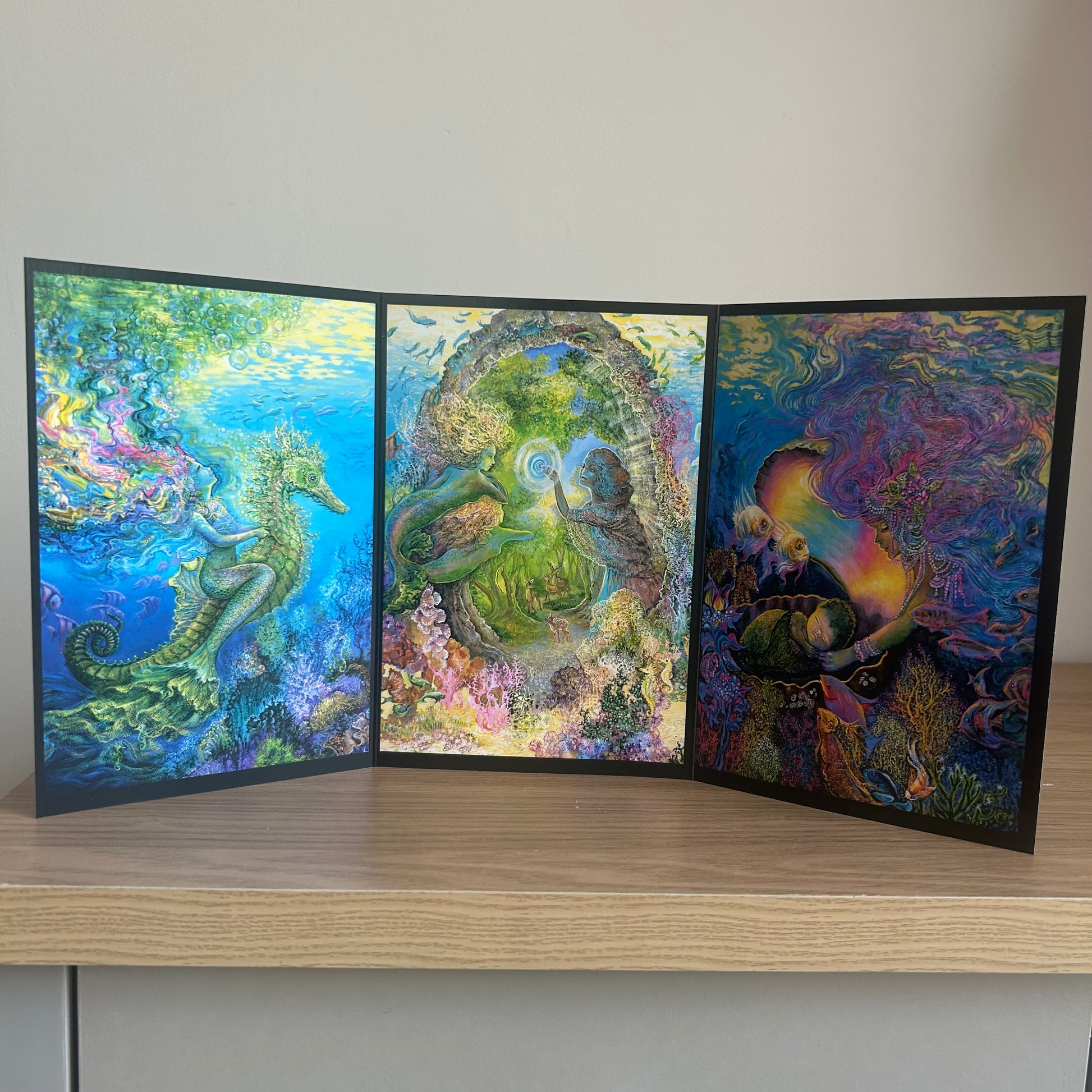 Three-panel self-sealing greetings card UK with artistic designs of under the sea and mermaid figures on a wooden surface.