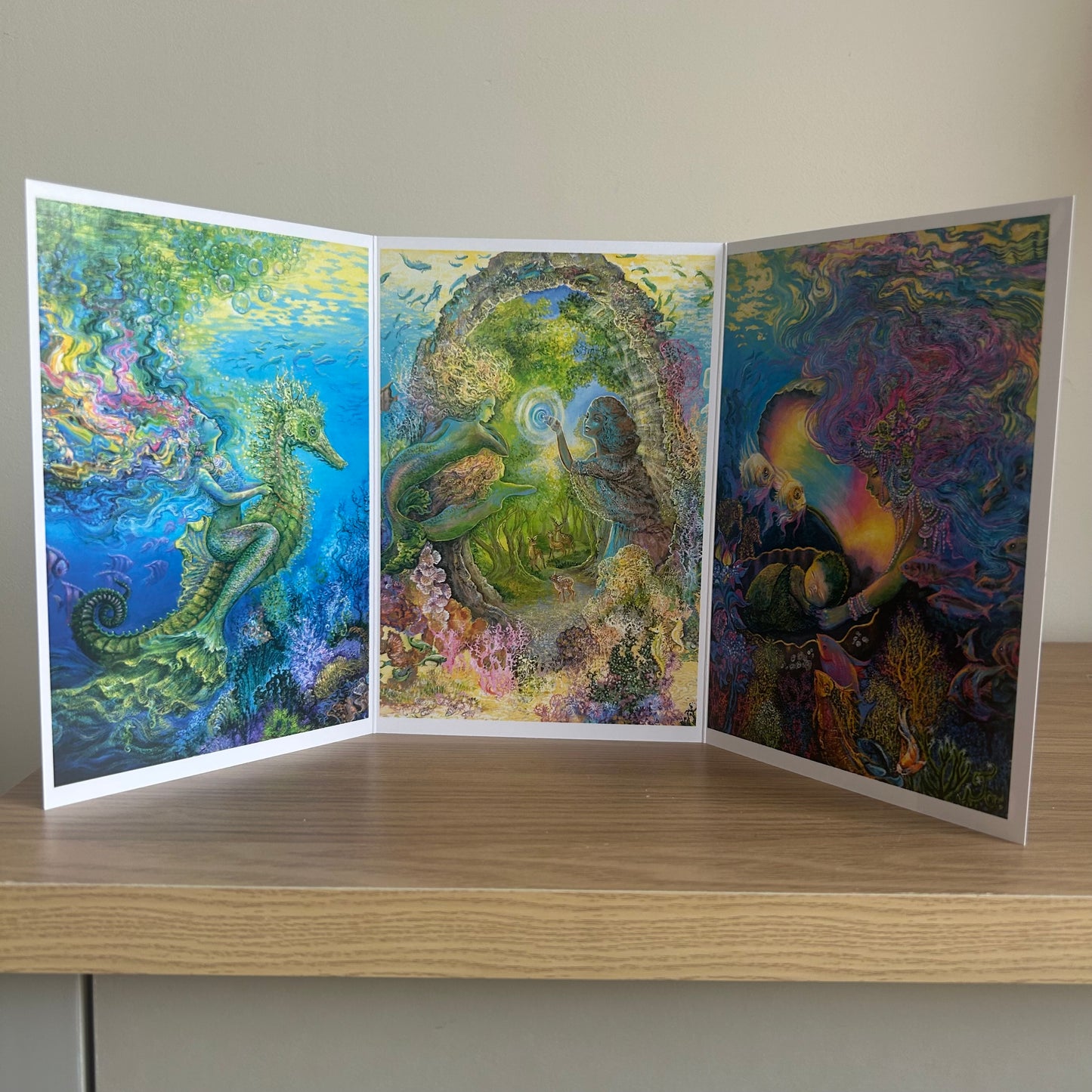 Three-panel self-sealing greetings card UK with artistic designs of under the sea and mermaid figures on a wooden surface.