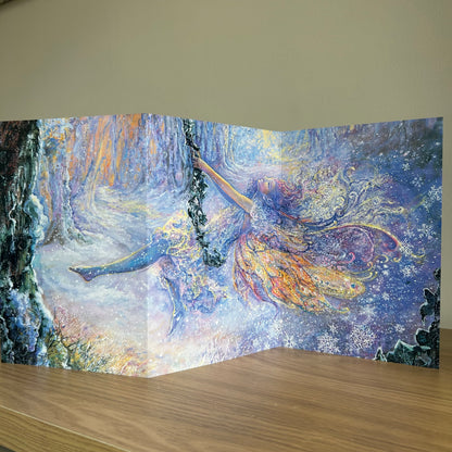 Trifold self-sealing greetings card featuring Fairy tale scene with a fairy swinging in the snow in a forest displayed on a shelf