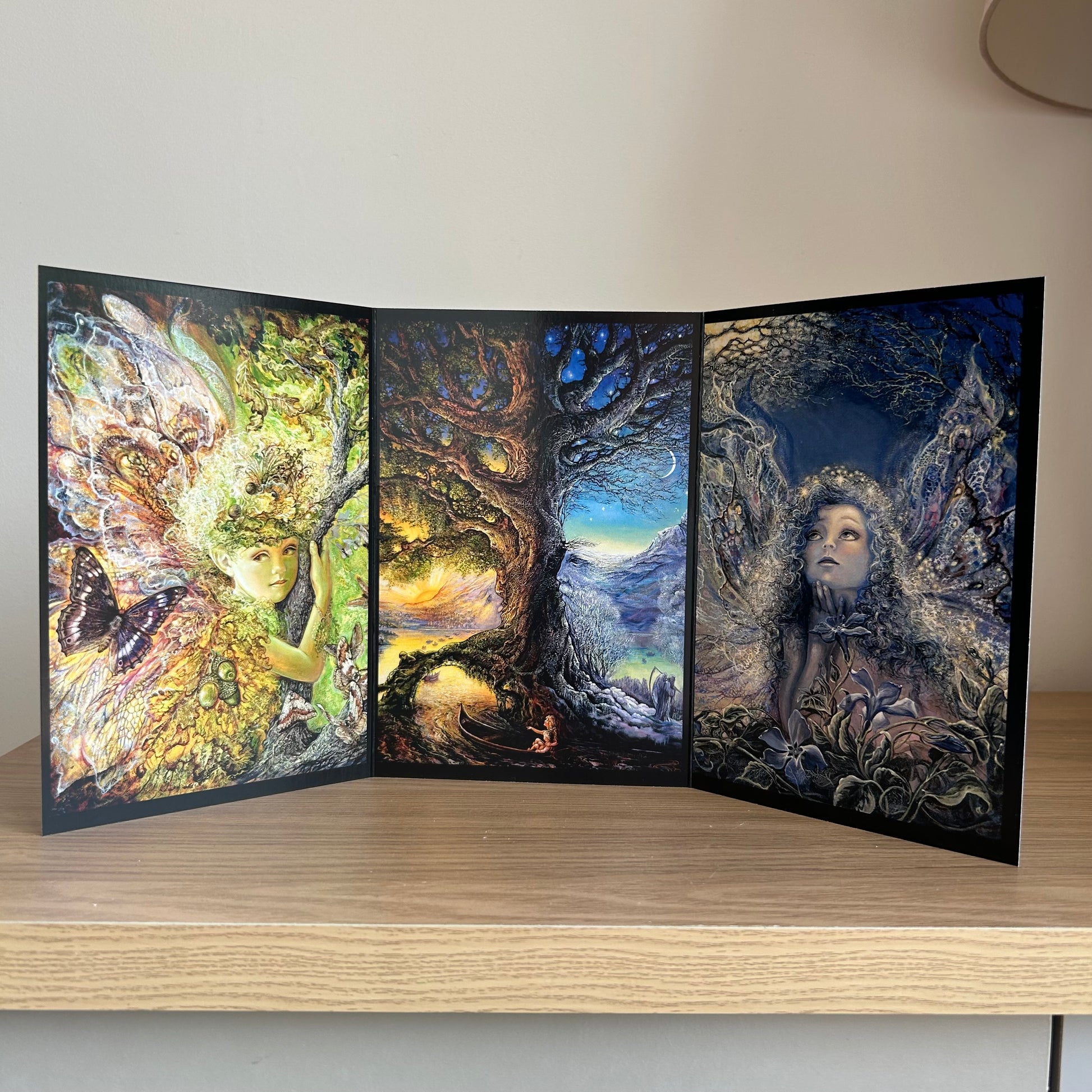 Three-panel self-sealing greetings card UK with artistic fantasy designs featuring Josephine Wall paintings of nature, fairies and mystical figures on a wooden surface