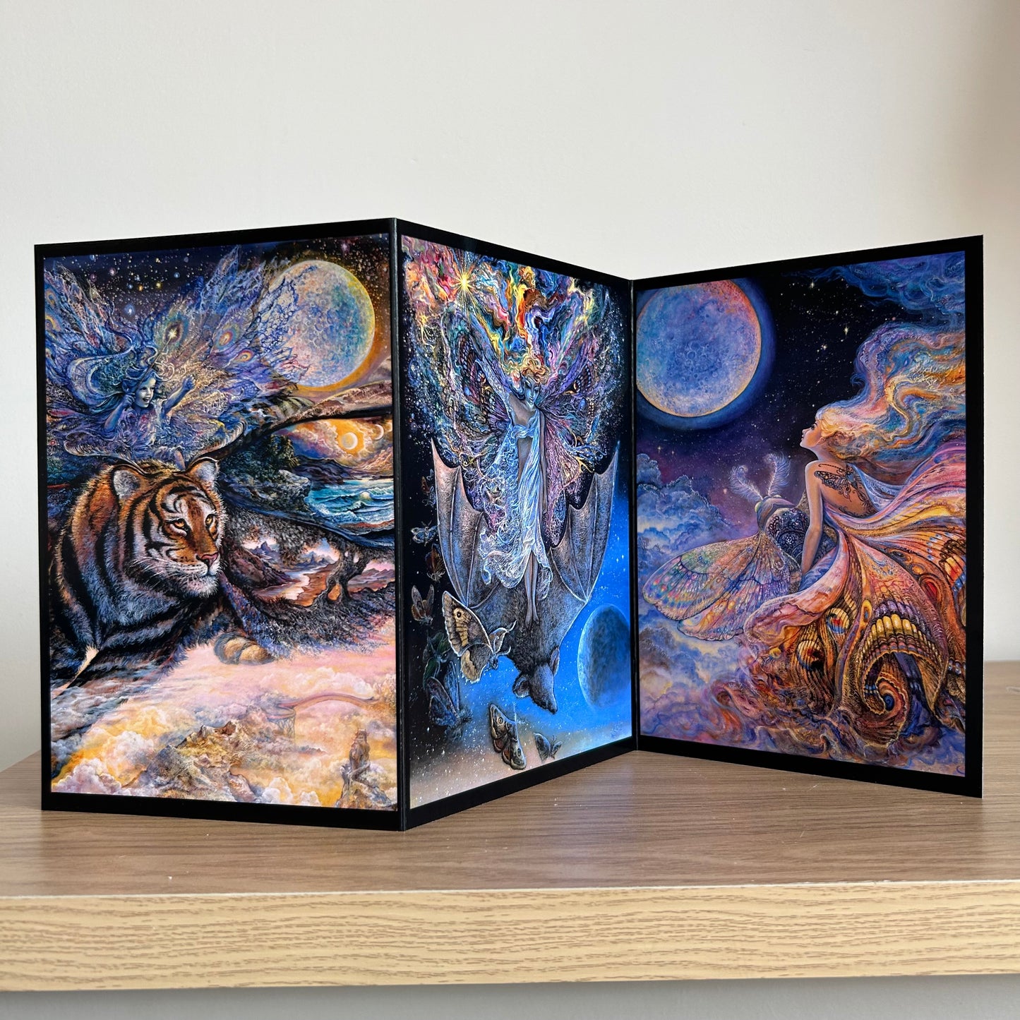 Three-panel self-sealing greetings card UK with artistic designs of fairy figures riding animals to the moon on a wooden surface.