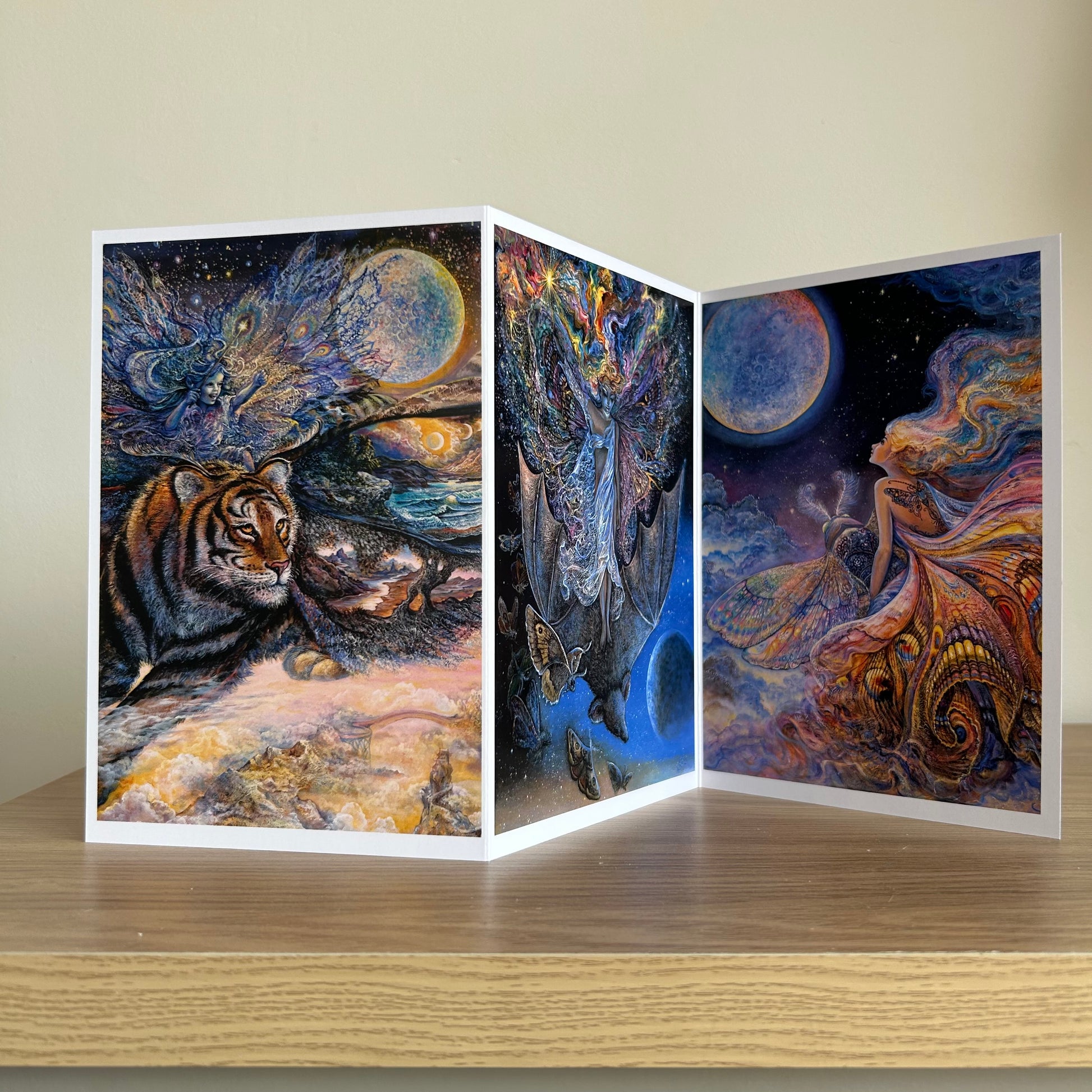 Three-panel self-sealing greetings card UK with artistic designs of fairy figures riding animals to the moon on a wooden surface.