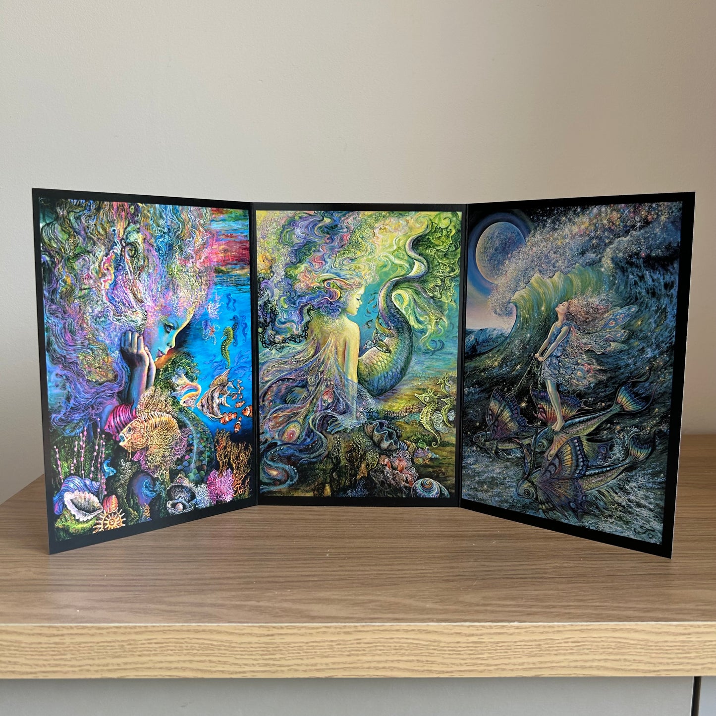 Three-panel self-sealing greetings card UK with artistic designs of under the sea and mermaid figures on a wooden surface.