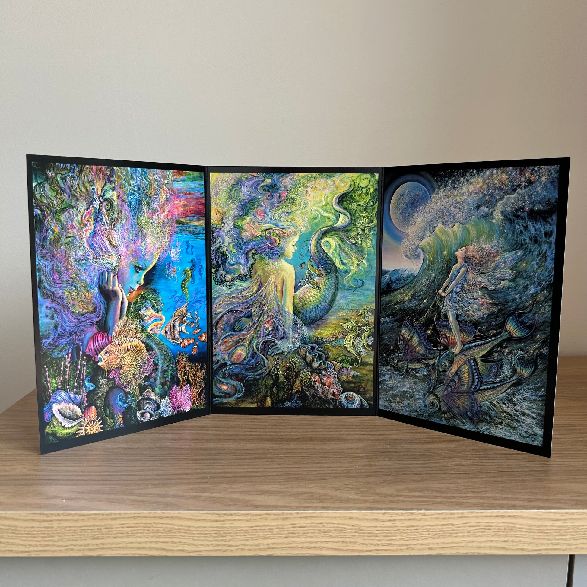 Three-panel self-sealing greetings card UK with artistic designs of under the sea and mermaid figures on a wooden surface.