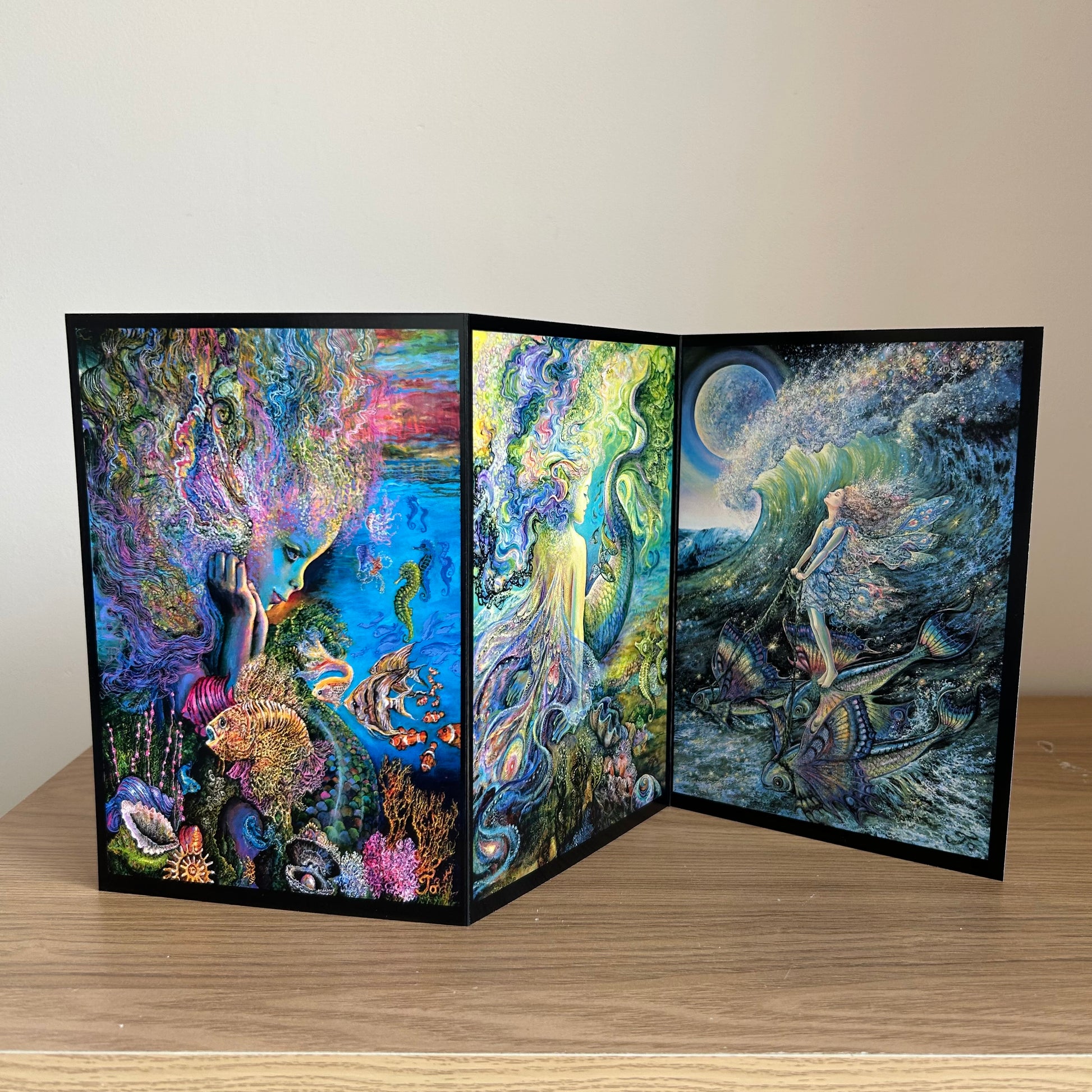 Three-panel self-sealing greetings card with artistic designs of under the sea and mermaid figures on a wooden surface.