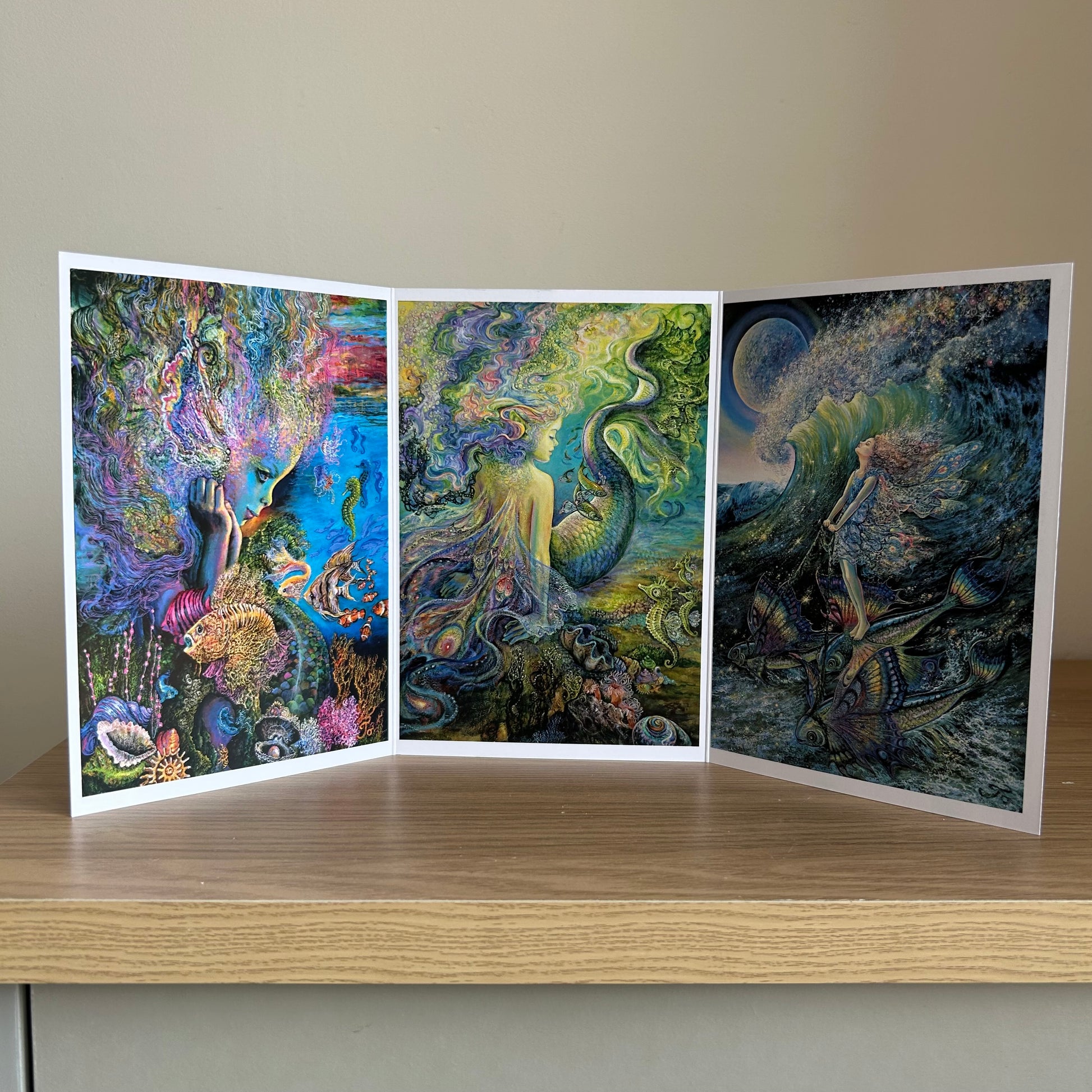 Three-panel self-sealing greetings card UK with artistic designs of under the sea and mermaid figures on a wooden surface.