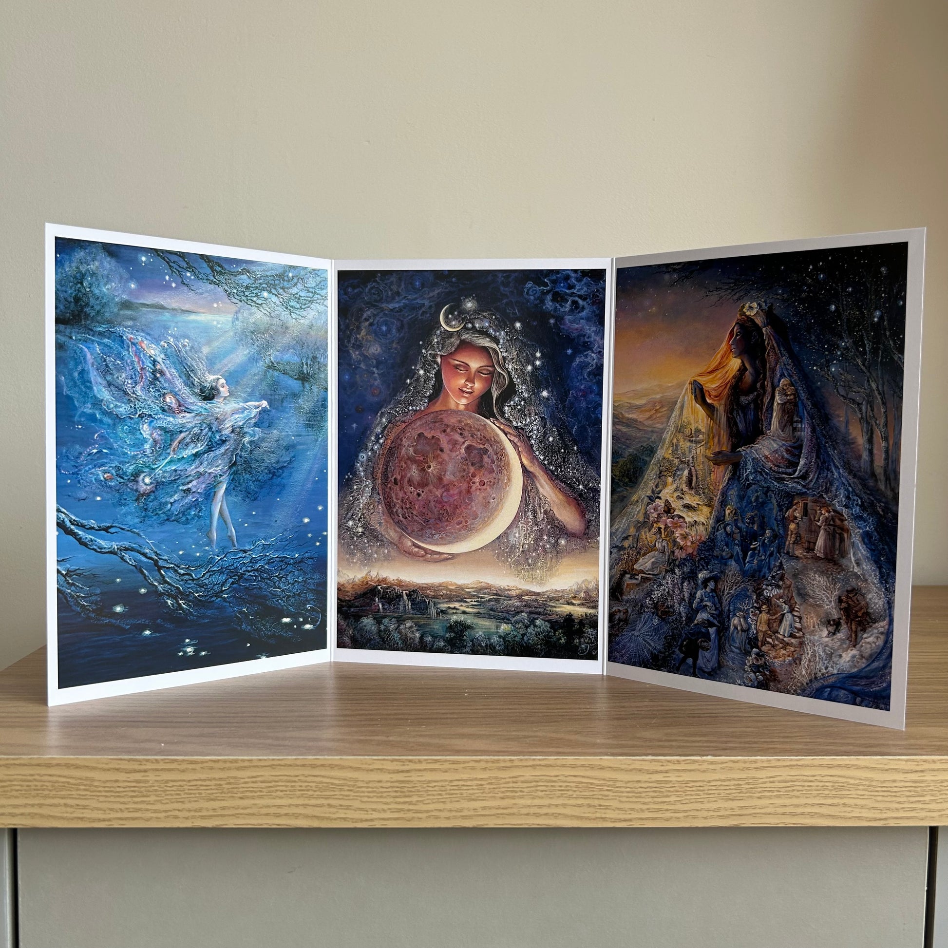 Three-panel self-sealing greetings card UK with artistic fantasy designs featuring Josephine Wall paintings of the moon and mystical fairies and goddesses on a wooden surface