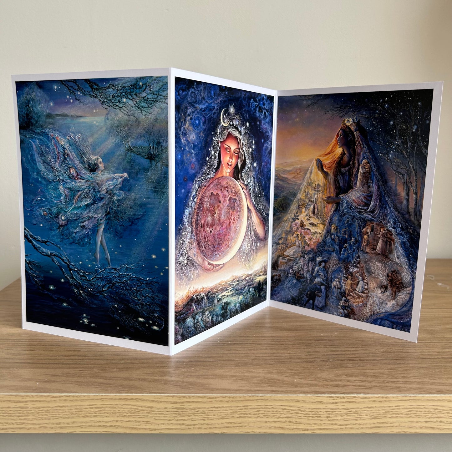 Three-panel self-sealing greetings card UK with artistic fantasy designs featuring Josephine Wall paintings of the moon and mystical fairies and goddesses on a wooden surface