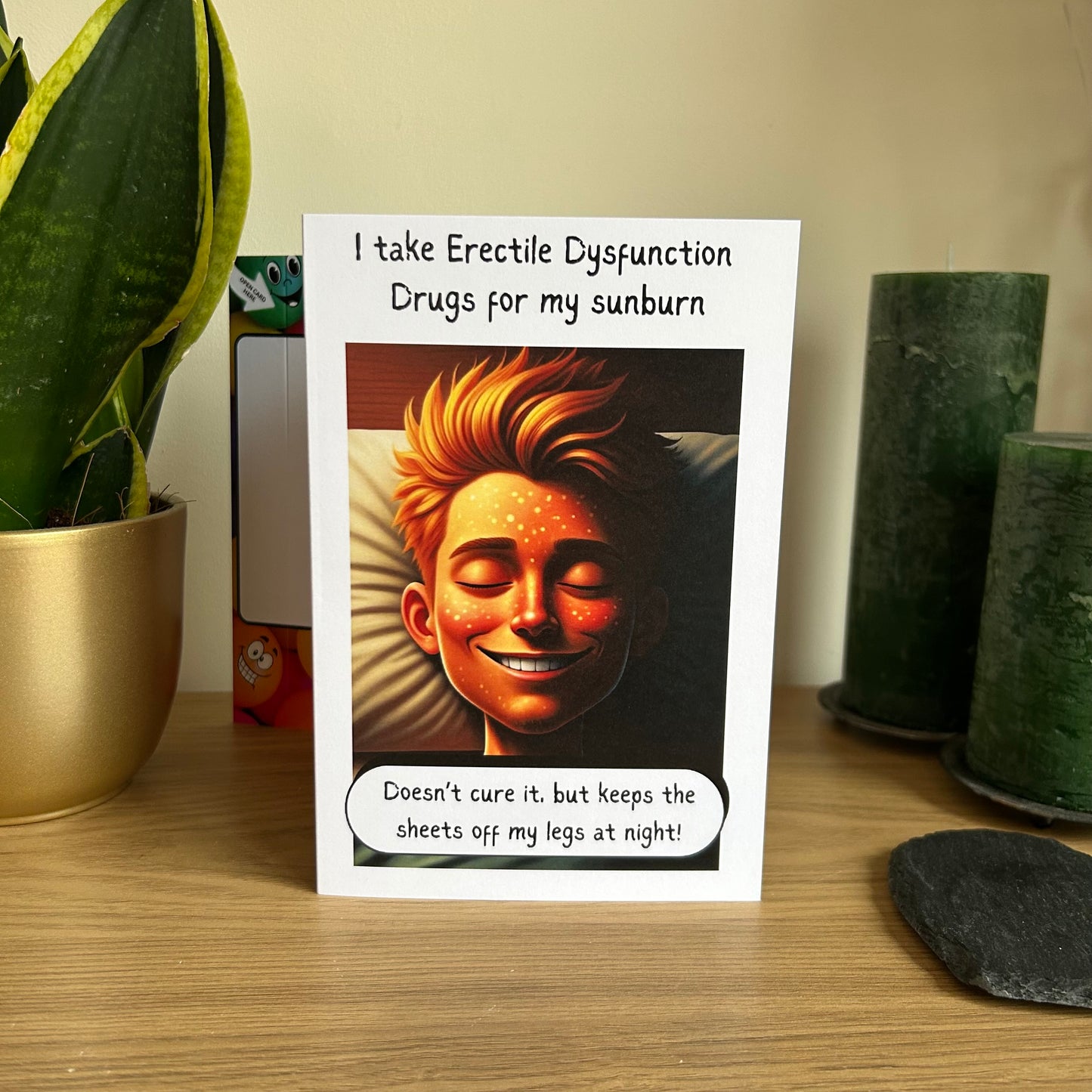 Image shows the Bare Cards Giggle Balls Humour Range 'Erectile Dysfunction Joke' Birthday Card displayed in a home setting. The illustration shows the headshot of a very satisfied man led in bed with the caption "I take Erectile Dysfunction Drugs for my sunburn. Doesn't cure it, but keep the sheets off my legs at night!"
