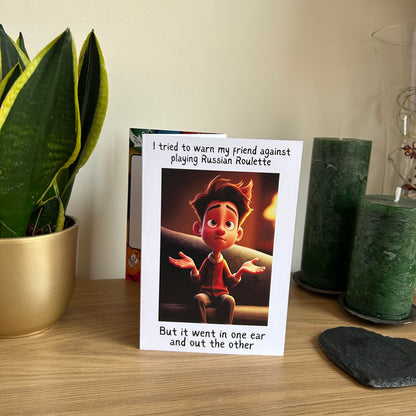 Image show the Bare Cards Giggle Balls Humour Range 'Russian Roulette Joke' Birthday Card displayed in a home setting. The illustration shows a man sat on a sofa holding his hands up, in resignation. The caption reads 'I tried to warn my friend against playing Russian Roulette But it went in one ear and out the other'