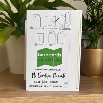 The back of the Bare Cards Happy Parent's Day self-sealing card showing step-by-step envelope folding instructions, photographed standing on a wooden surface between two potted green plants.