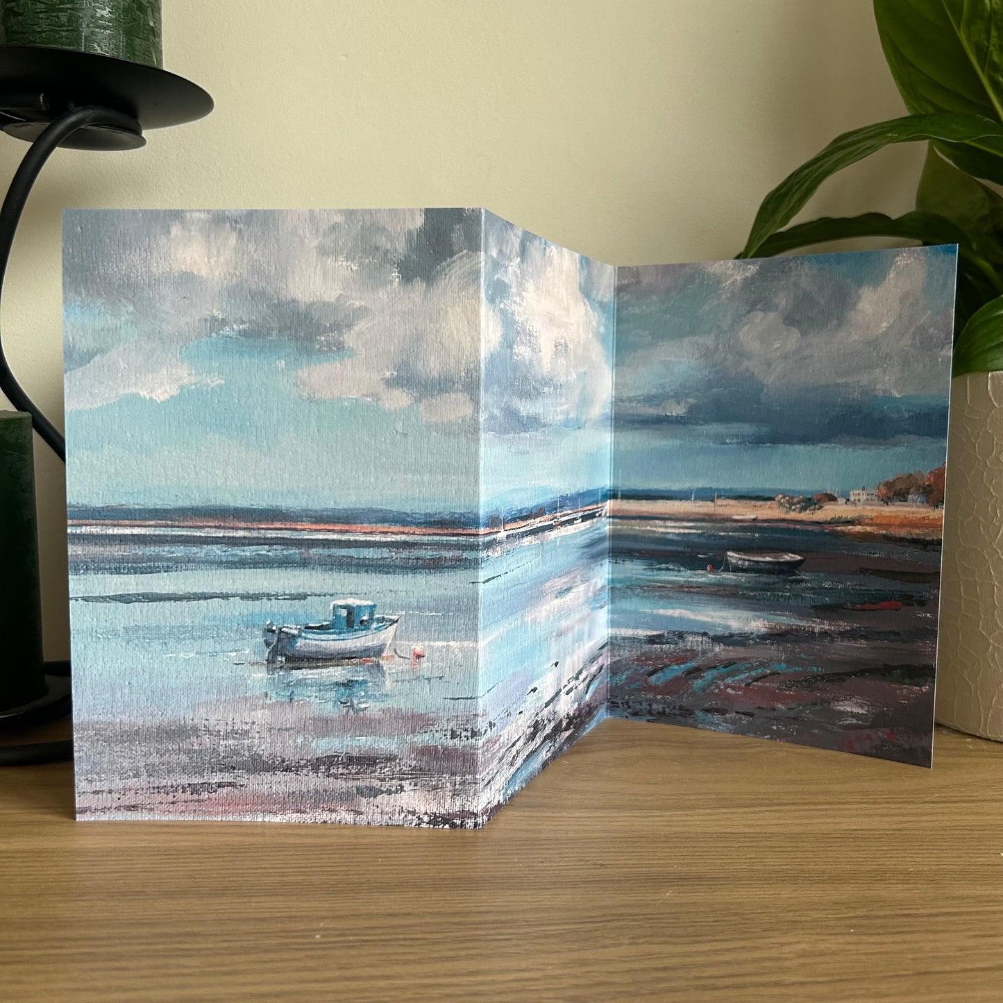Tri-fold card with a scenic painting of a boat on water, displayed on a wooden surface.