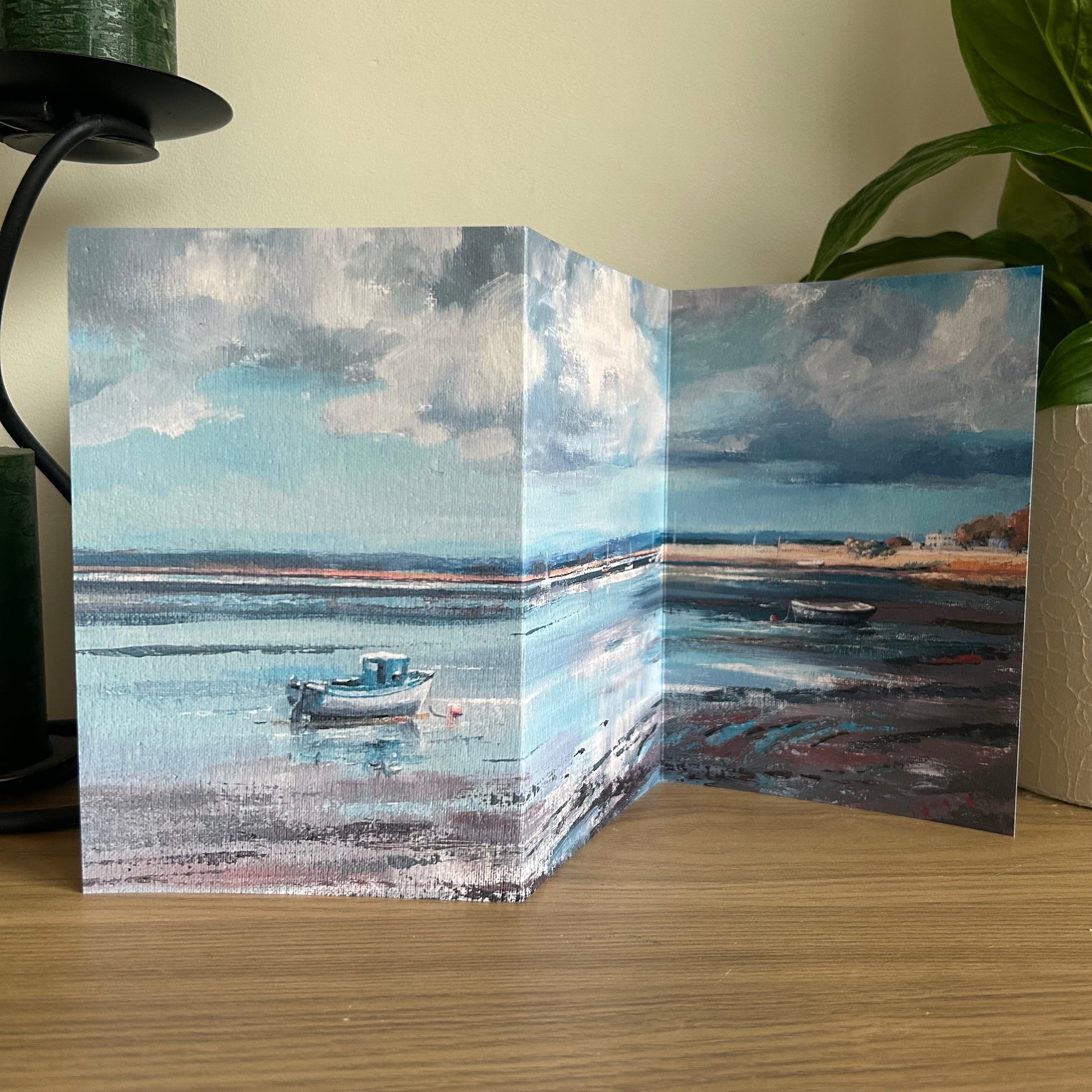 Tri-fold card with a scenic painting of a boat on water, displayed on a wooden surface.