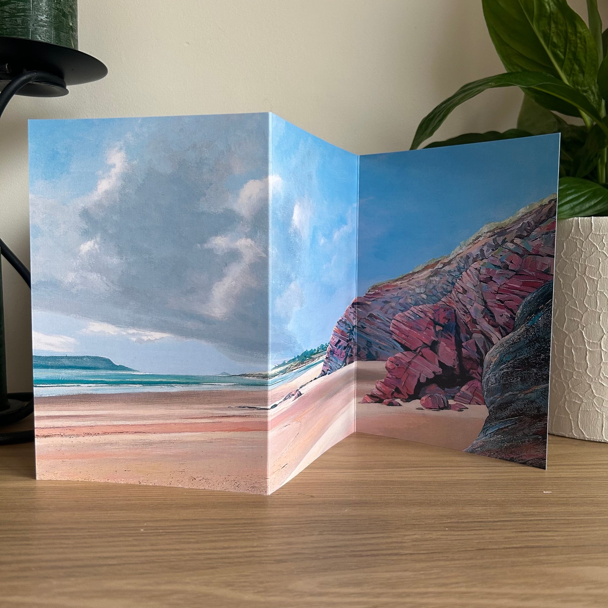Folded beach scene card with ocean and cliffs on a wooden surface.