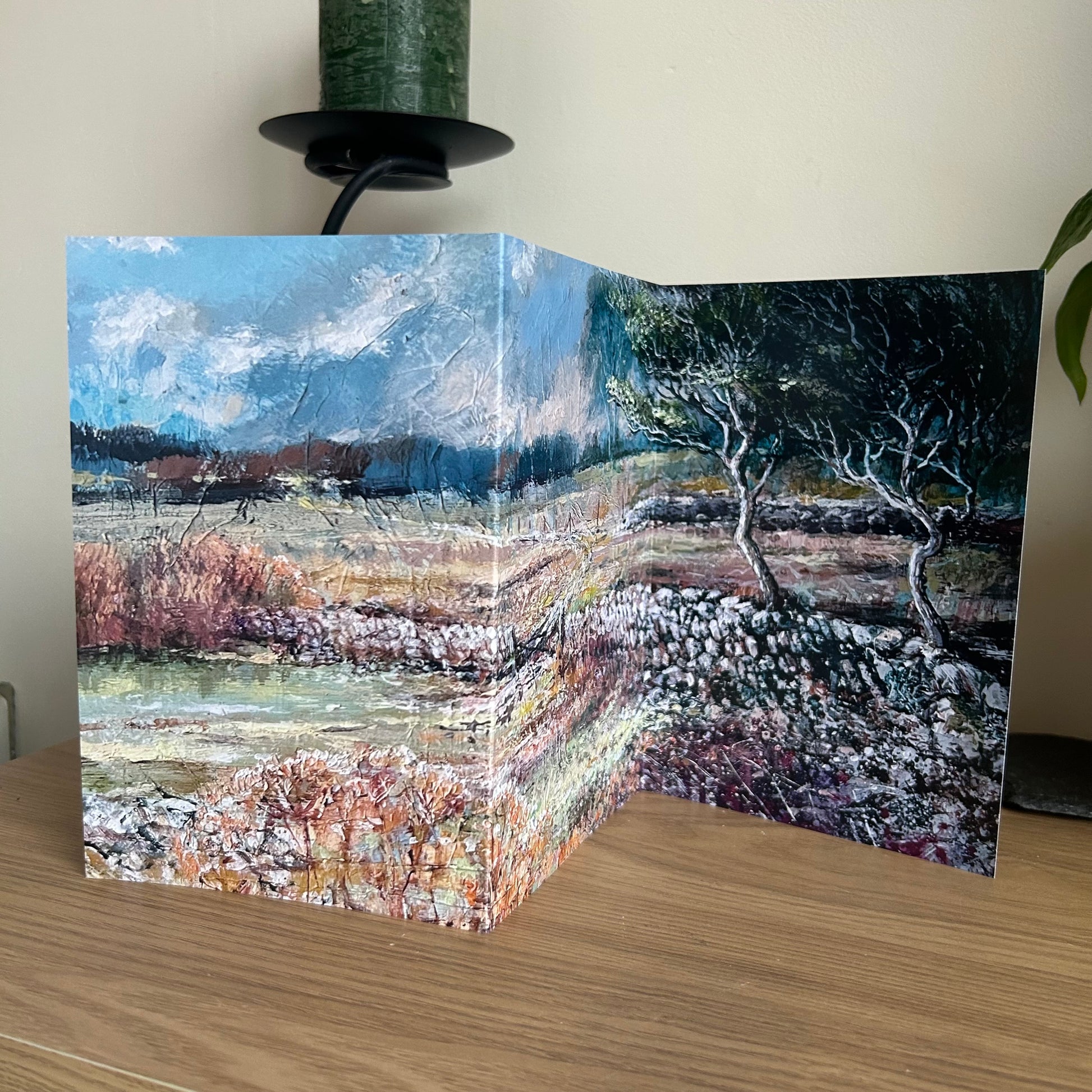 self-sealing trifold greetings card with artistic depiction of a landscape with trees and water on a wooden surface.
