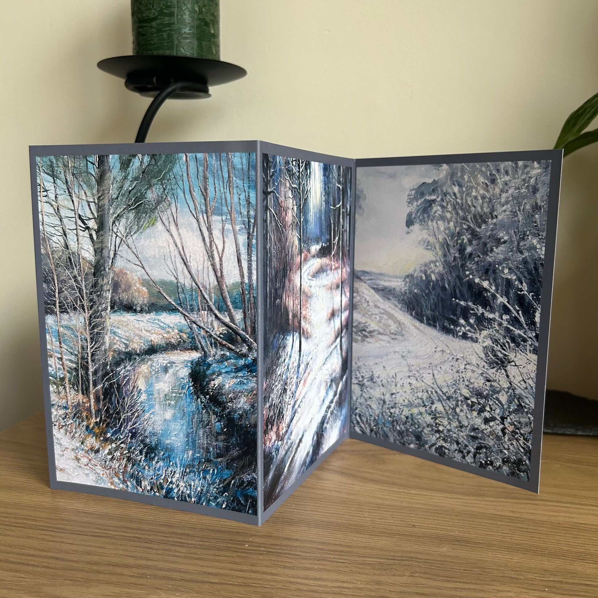 Foldable card with winter landscape design on a wooden surface.