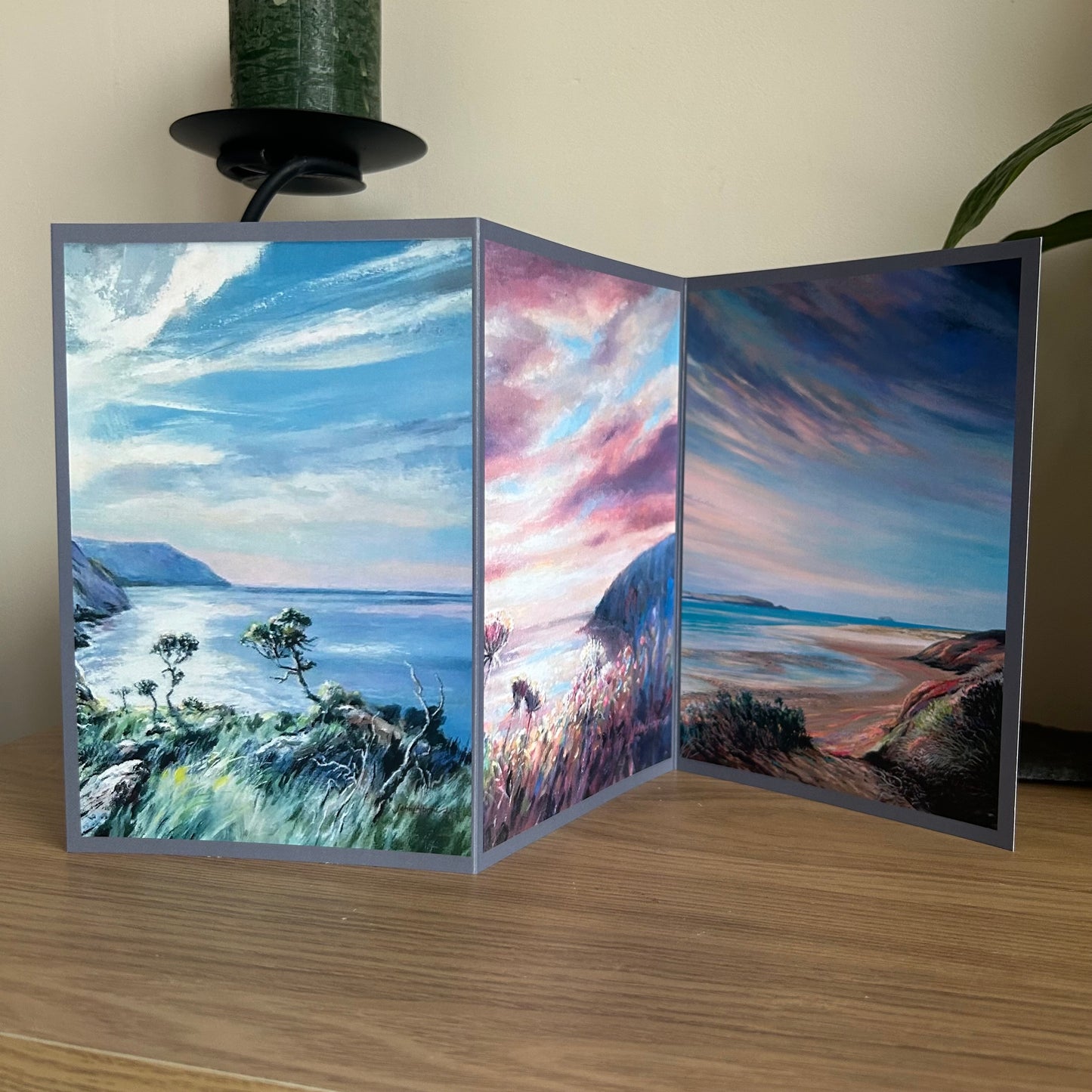 Trifold greetings card showing a triptych painting of coastal scenes on a wooden surface
