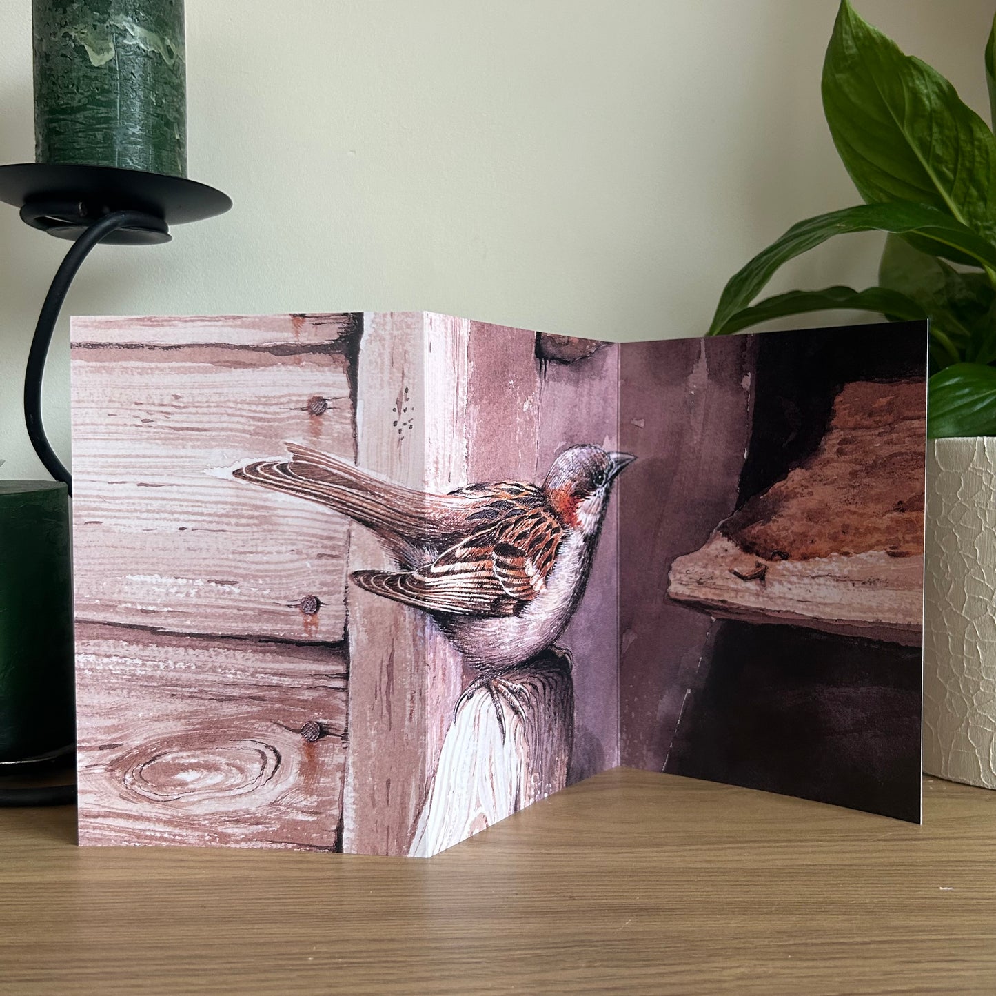 Trifold Greeting card with a sparrow design on a wooden surface with a plant and candle in the background.