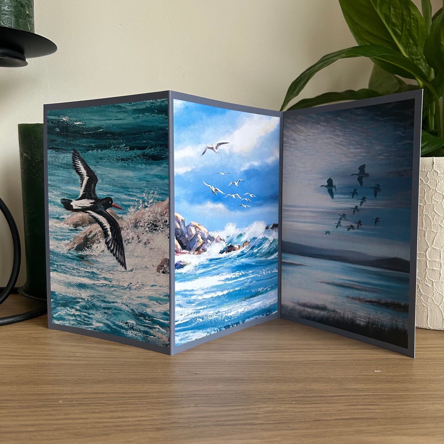 Tri-fold card with ocean and bird designs on a wooden surface.