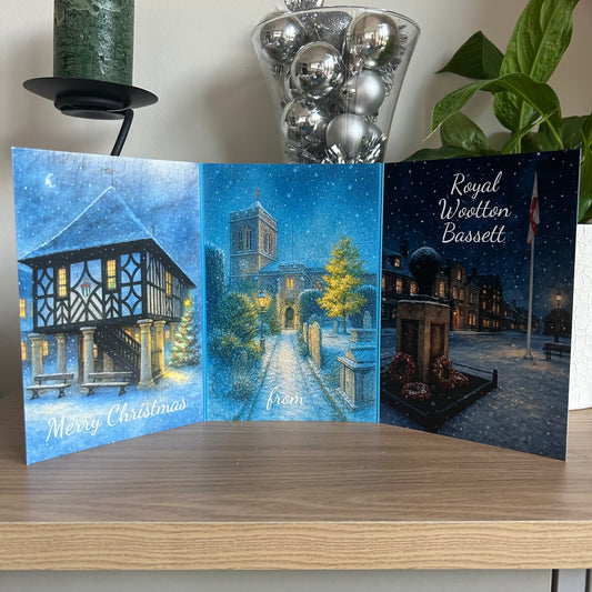 Christmas card with festive village scene, candle, and decorative balls on a wooden surface.