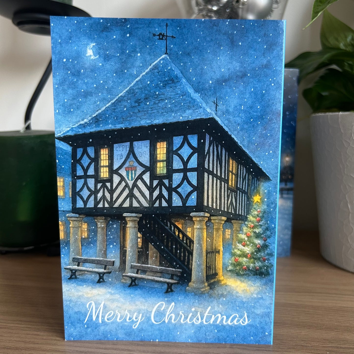 Christmas card with a festive house and tree design on a blue snowy background.