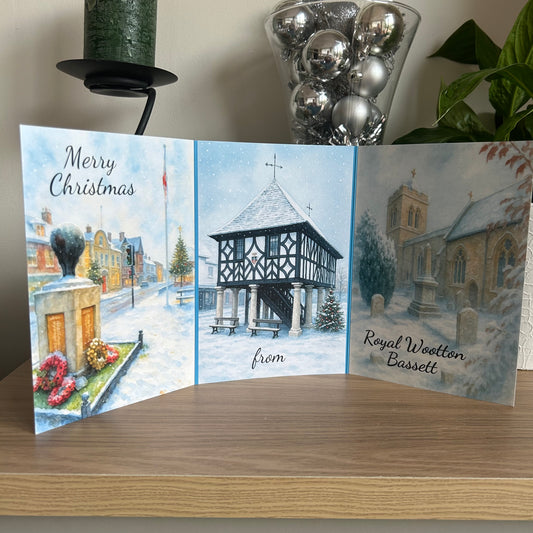 Christmas card with snowy village scene, church, and festive elements on a wooden surface.