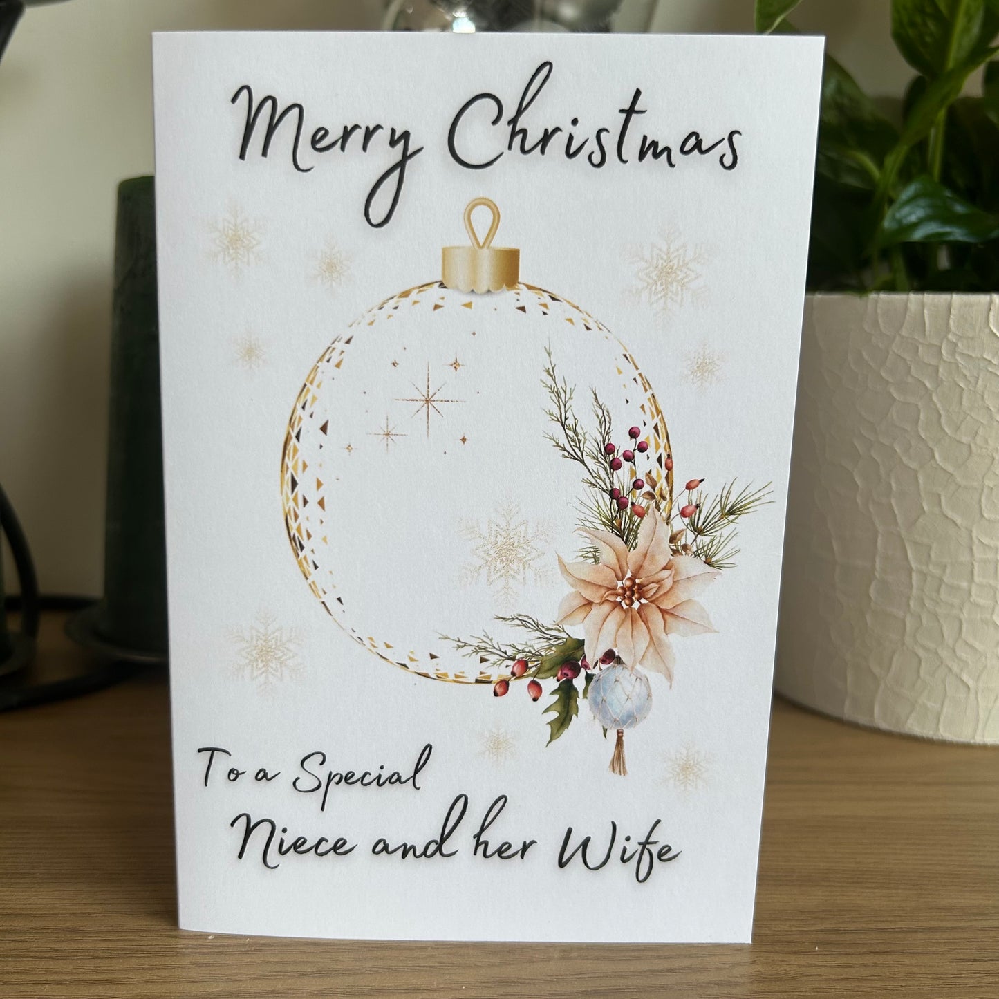 Christmas card with floral ornament design and personalized message on a wooden surface.