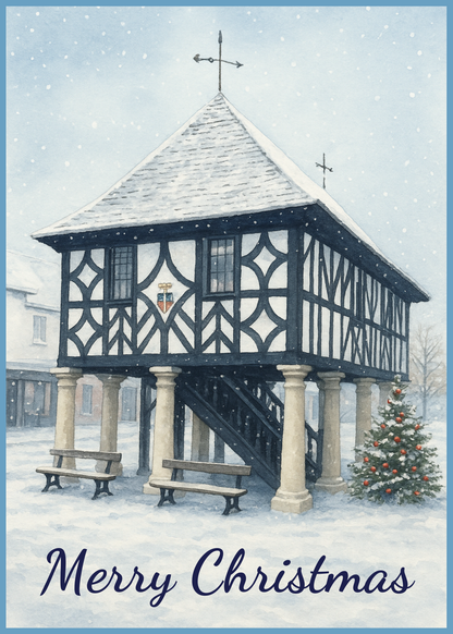A festive Christmas greeting card featuring a winter illustration of a historic black-and-white timber-framed building in snow, with two benches, a decorated Christmas tree, and the text 'Merry Christmas' at the bottom.