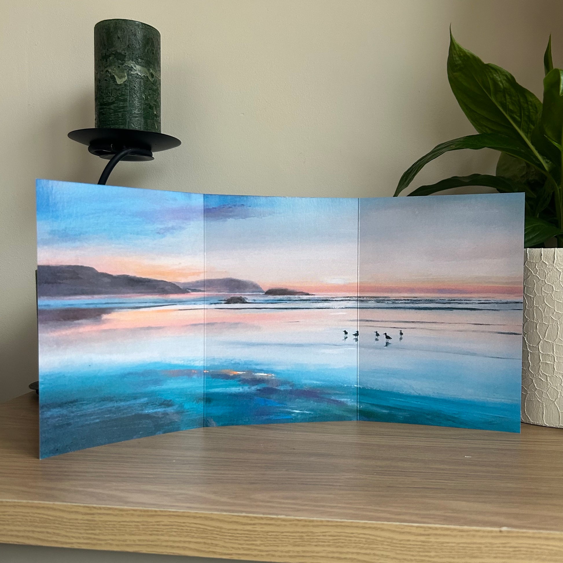 Trifold greetings card featuring a painting of the sunset over Polzeath beach in Cornwall on a wooden surface.