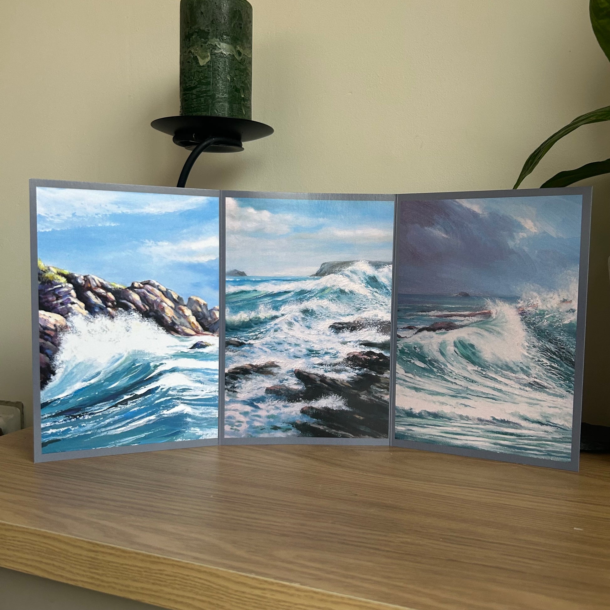Self-sealing greetings card featuring Triptych paintings of ocean waves on a wooden surface with a plant in the background.