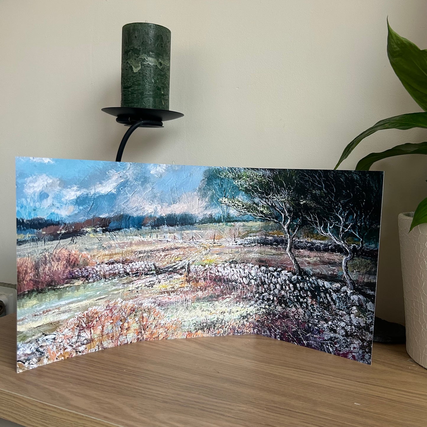 Greetings card showing artistic landscape print on a wooden surface with a candle and plant in the background