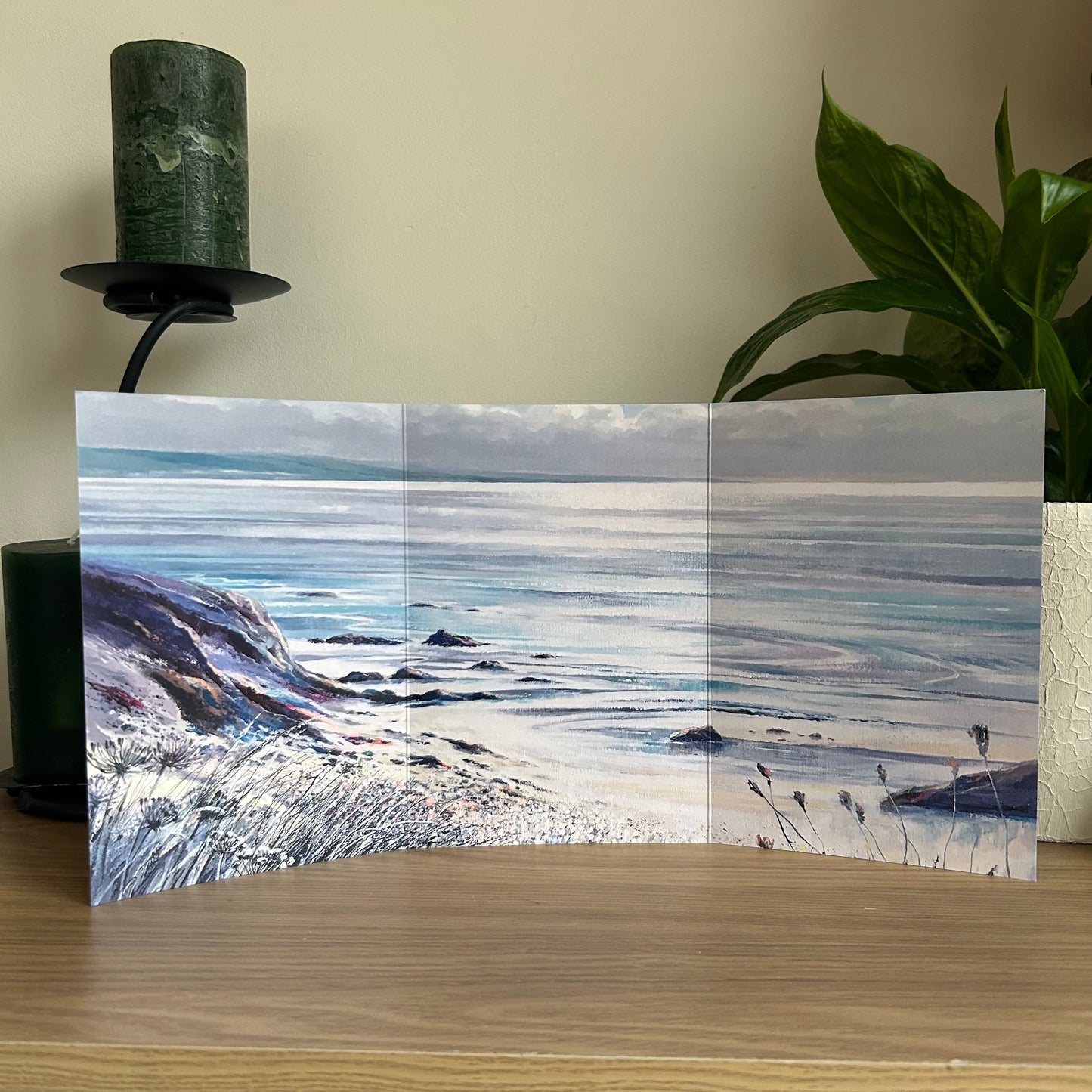 Scenic trifold greetings card with a beach and ocean view on a wooden surface.