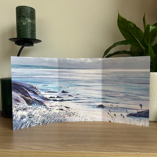 Scenic trifold greetings card with a beach and ocean view on a wooden surface.